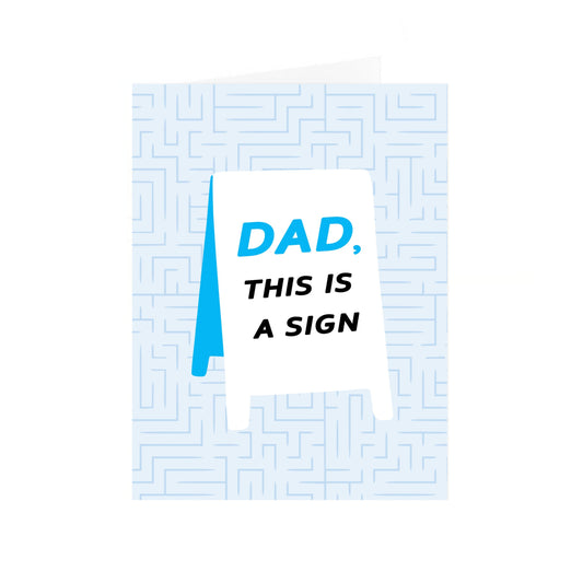 A folded greeting card with a light blue background filled with a subtle, geometric maze pattern. On the front of each card is a white A-frame sidewalk sign. The text printed on the sign reads: "Dad," in blue, followed by "This is a sign" in bold black capital letters. The card is standing upright and slightly open.