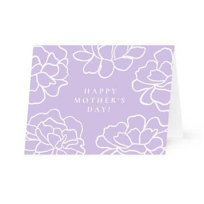 A horizontal greeting card with a light purple background featuring white, line-art illustrations of large peony-like flowers blooming from the corners and top edge. Centered in the middle of the card, the all caps words "Happy Mother's Day!" are written in a clean, white, serif font. The card is shown slightly propped open against a plain white background.