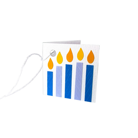 Paper gift tag with five paper candles in purple and blue, each topped with a yellow flame. The gift tag is attached by a white string.