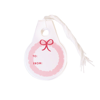 This is a set of ten white paper gift tags that are shaped like a big circle with a little square handle at the top. In the middle of the tag, there is a  pink circular garland that looks like a Christmas wreath. Right on top of the pink wreath sits a bright red bow. On the side, it says "To:" and "From:" in red letters so you know exactly who the present is for. Each tag has a white string at the top so you can tie it onto a gift. The ten tags are stacked and centered on a white background.