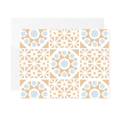A horizontal greeting card featuring an all-over pattern of tan-colored Mediterranean tiles arranged in a symmetrical grid format. The folded card is shown laying flat with a white envelope tucked behind it. The card is centered against a plain white background.