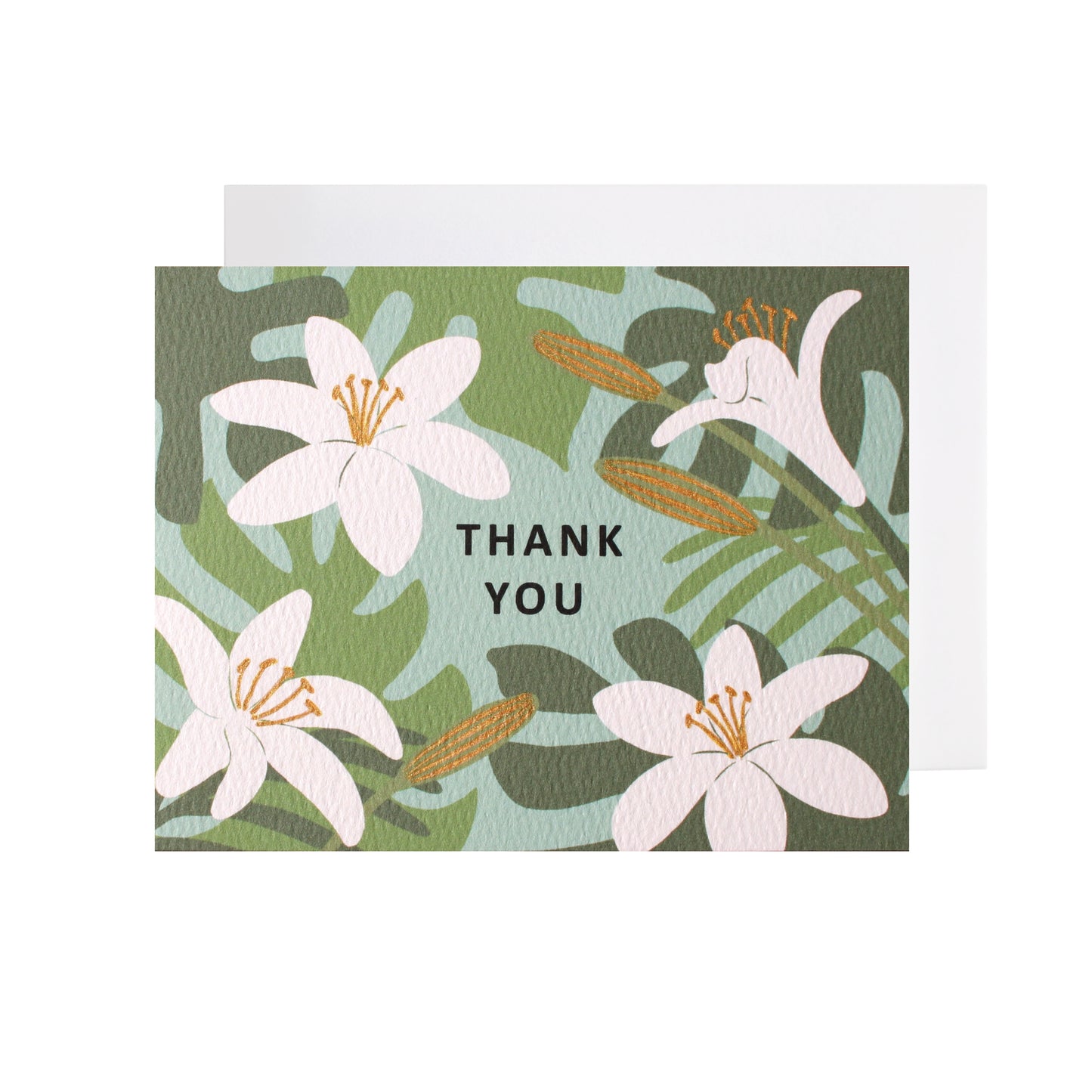 A folded horizontal thank you card resting flat on a white surface with a white envelope tucked underneath. The card features an illustrated pattern of white lilies and green tropical leaves against a light teal-blue background. The words "thank you" are centered in black capital letters. Some floral elements are accented with metallic gold-colored ink.