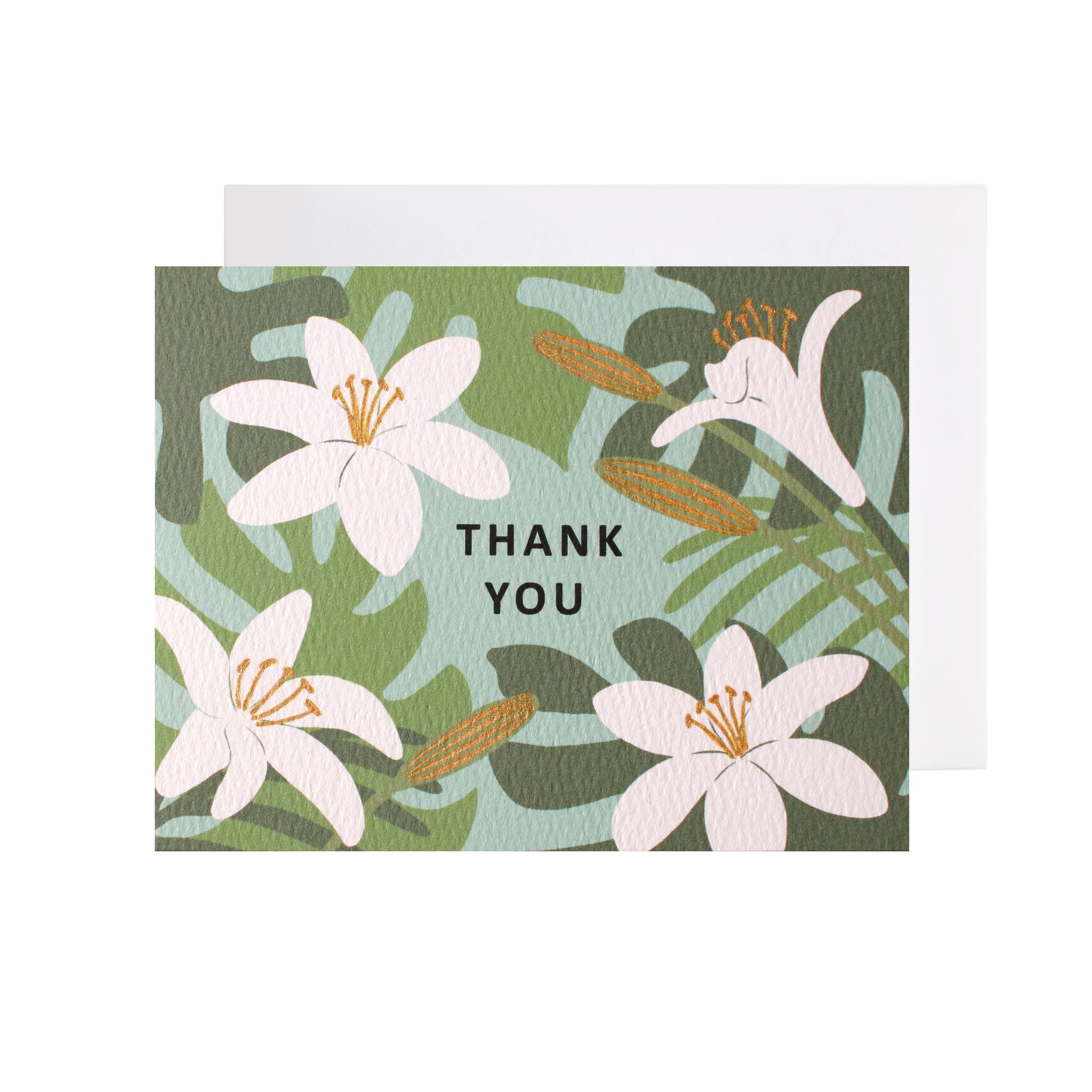 A folded horizontal thank you card resting flat on a white surface with a white envelope tucked underneath. The card features an illustrated pattern of white lilies and green tropical leaves against a light teal-blue background. The words "thank you" are centered in black capital letters. Some floral elements are accented with metallic gold-colored ink.