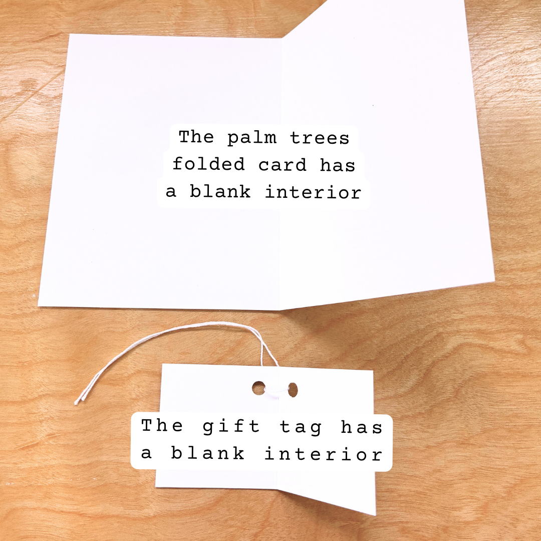 A folded white greeting card and a matching gift tag laid on a light wood surface. Both pieces of paper have black typewriter-style text reading, 'The palm trees folded card has a blank interior' and 'The gift tag has a blank interior' respectively.