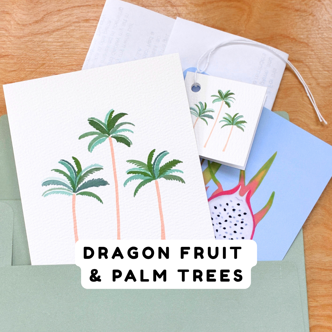 A set of tropical-themed stationery cards fanning out of a green envelope on a wooden surface. The main card features three green palm trees on a white background, with a matching small gift tag.