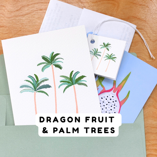 A set of tropical-themed stationery cards fanning out of a green envelope on a wooden surface. The main card features three green palm trees on a white background, with a matching small gift tag.