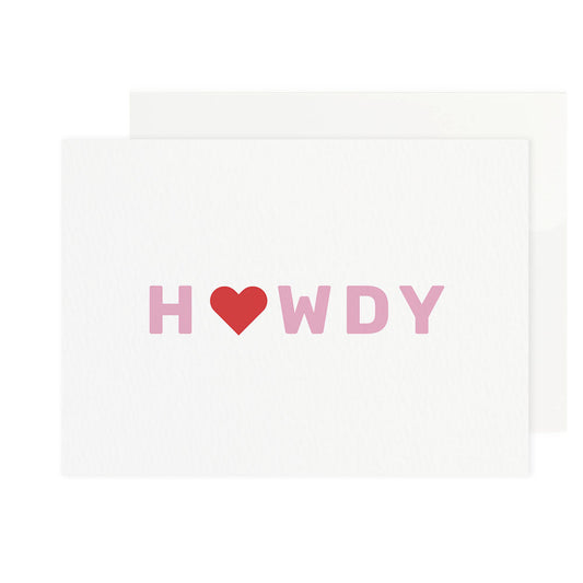 a white rectangular greeting card centered on a white background with a matching white envelope tucked behind it. the word howdy is printed across the center of the card in pink capital letters, with a solid red heart symbol used in place of the letter o.