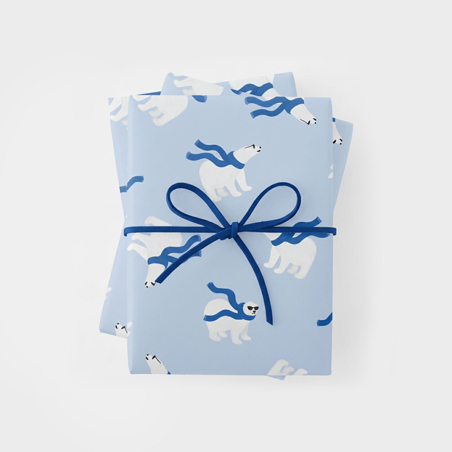 a top-down view of a rectangular gift wrapped in light blue paper featuring a repeating pattern of white polar bears wearing dark blue scarves and sunglasses. the gift is tied with a thin, dark blue cord in a simple bow at the center.