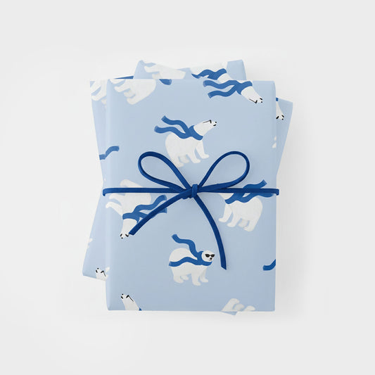 a top-down view of a rectangular gift wrapped in light blue paper featuring a repeating pattern of white polar bears wearing dark blue scarves and sunglasses. the gift is tied with a thin, dark blue cord in a simple bow at the center.