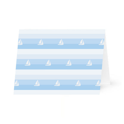 A single notecard featuring a pattern of horizontal blue stripes and white sailboats. The patterned horizontal card is standing propped open and it is centered on a white background.